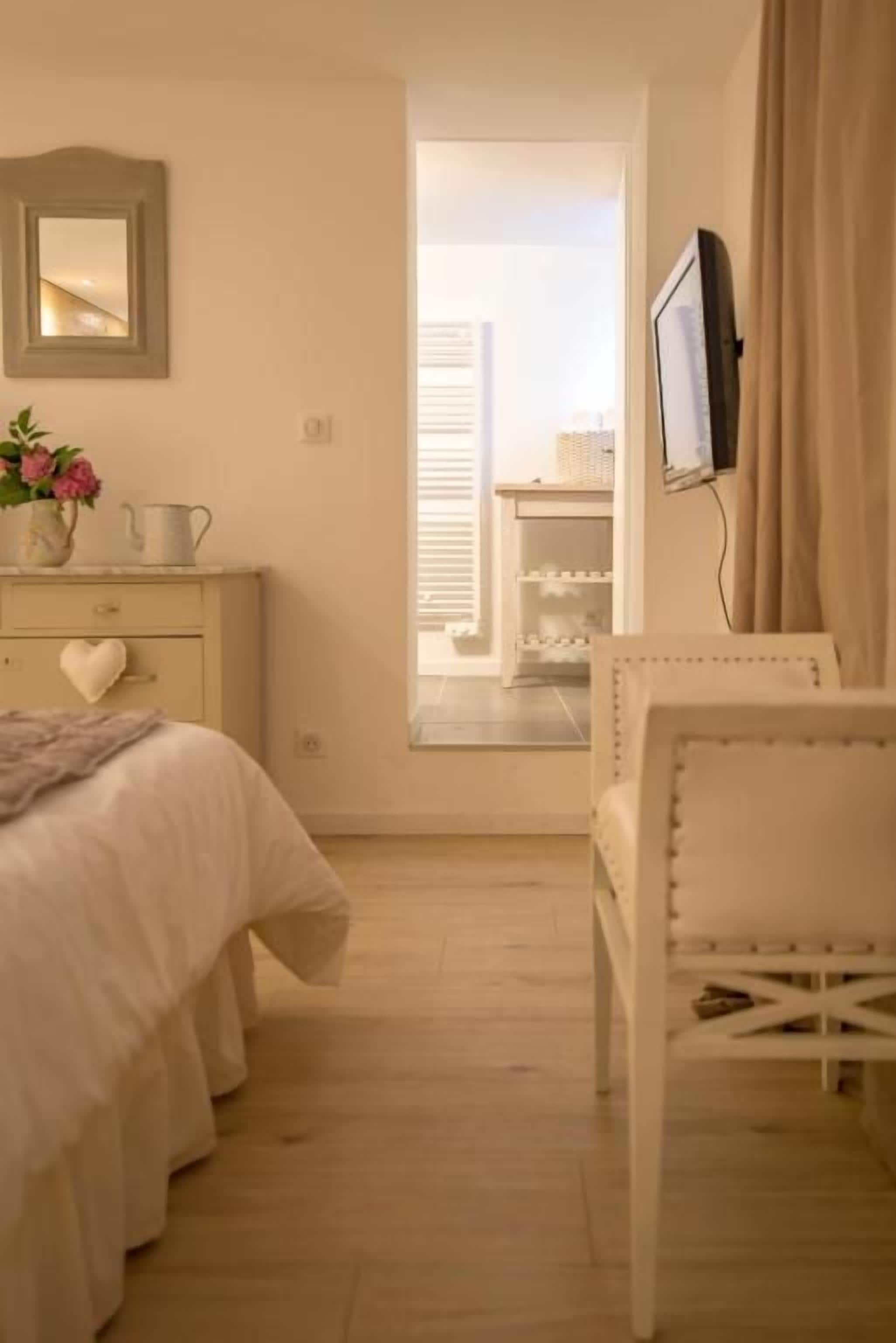 Een slaapkamer met een bed, een dressoir, een aan de muur bevestigde televisie en een raam met gordijnen.