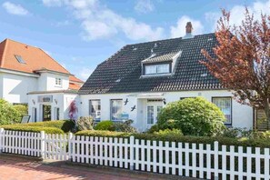 Ein weißes Gebäude mit einem schwarzen Dach, einem weißen Zaun und einem gepflegten Garten.