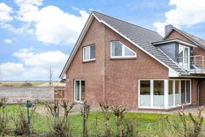 Ein zweistöckiges Haus mit geneigtem Dach, großen Fenstern und einem Balkon.