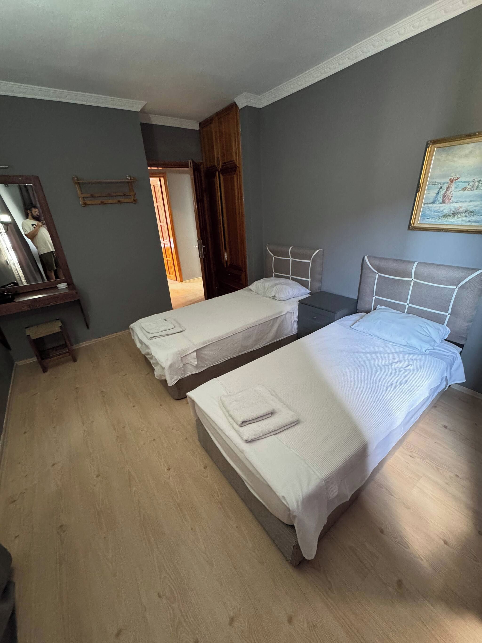 Quarto de hotel com duas camas, piso de madeira, espelho e um quadro na parede.