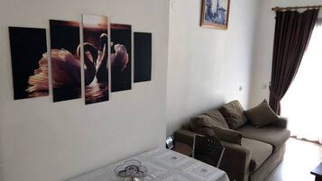 Un salon comprenant un canapé, une table à manger agrémentée d’un centre de table en verre et des œuvres d’art murales.