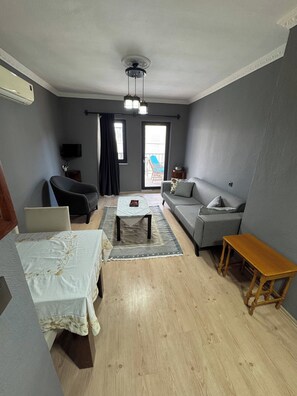 A living room with a sofa, a small table, a coffee table, a TV, and a balcony door. - Charming 2-Bedroom Apartment with Shared Pool in Kalkan center (Kaş)