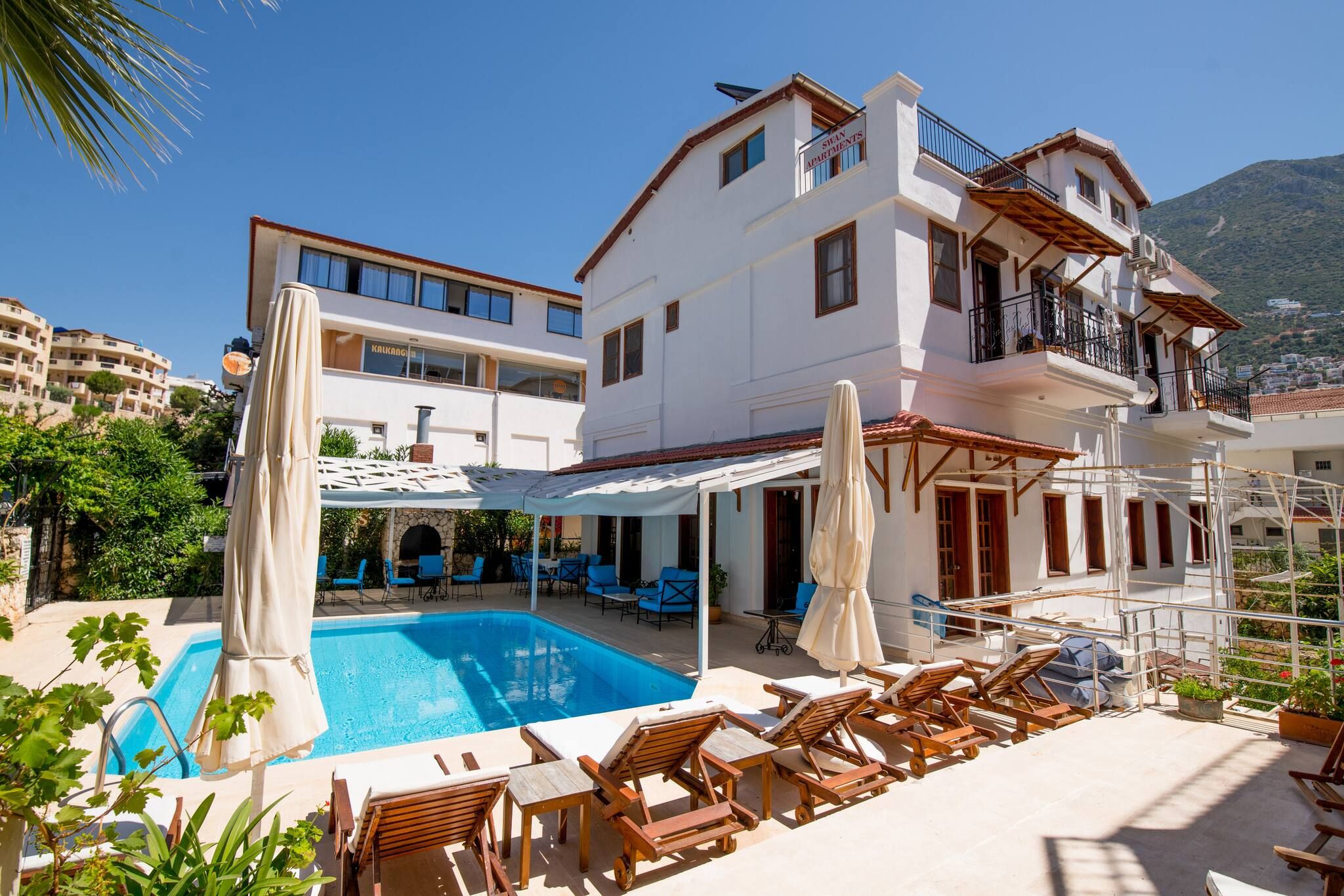 Um edifício de dois andares com piscina, área de estar ao ar livre e montanhas ao fundo.