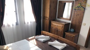 Ein Hotelzimmer mit einem Bett, einem hölzernen Schminktisch, einem Spiegel und einem fenster mit Vorhängen.