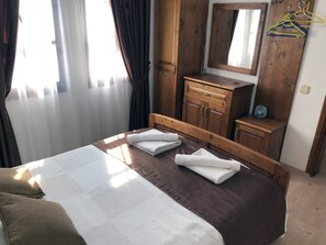 A hotel room with a bed, a wooden dresser, a mirror, and a window with curtains. - Charming 2-Bedroom Apartment with Shared Pool in Kalkan center (Kaş)