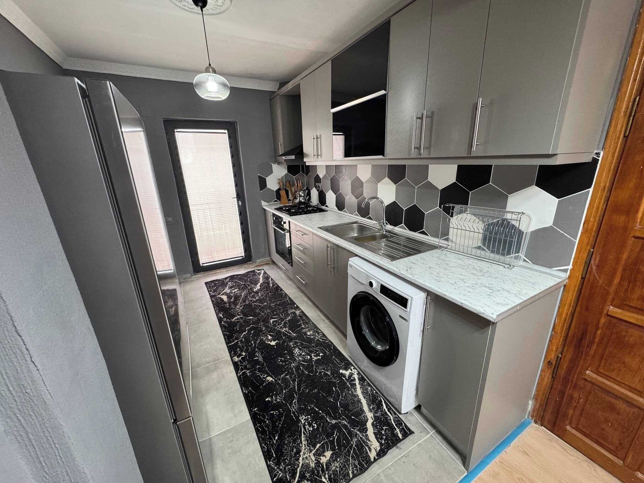 Cozinha moderna com armários cinzas, máquina de lavar e painel de azulejos hexagonais.