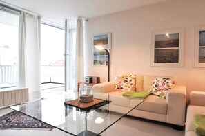 A modern living room with a glass coffee table, a sofa with floral cushions, and artwork on the walls. - 11 in the house at Blanker-Hans-Weg 5 (ID 081) (St. Peter-Bad)