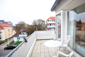 A balcony with a white table and chairs, a green kayak, and a black car parked outside. - 11 in the house at Blanker-Hans-Weg 5 (ID 081) (St. Peter-Bad)