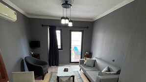 Una sala de estar con un sofá, una mesita, una mesa de centro, un televisor y una puerta con acceso a un balcón.