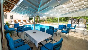 Un área de piscina al aire libre con sillas y una mesa azules, rodeada por un porche cubierto.