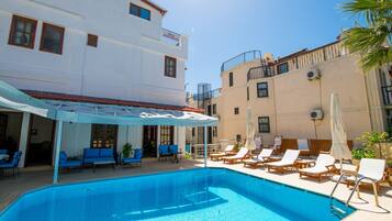 A swimming pool with lounge chairs and a covered seating area, surrounded by buildings with balconies.