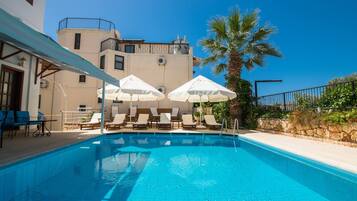 A swimming pool with lounge chairs and umbrellas, surrounded by a building with a balcony.