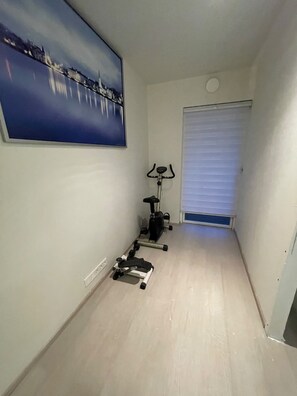 Ein schmaler Flur mit einem an der Wand hängenden Gemälde, einem stehenden Ergometer und einer Tür mit Fenster.