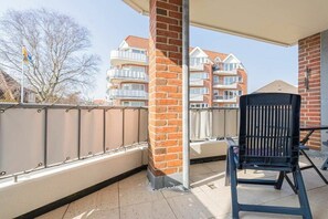 A balcony with a black chair, a brick pillar, and a view of multi-story buildings. - 3 in the house at Blanker-Hans-Weg 5 (ID 352) (St. Peter-Ording)