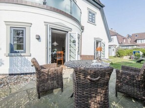 A white building with a curved exterior, a round wicker table, and wicker chairs in the outdoor seating area. - Holiday Apartment in Westerland With Sauna (Sylt)