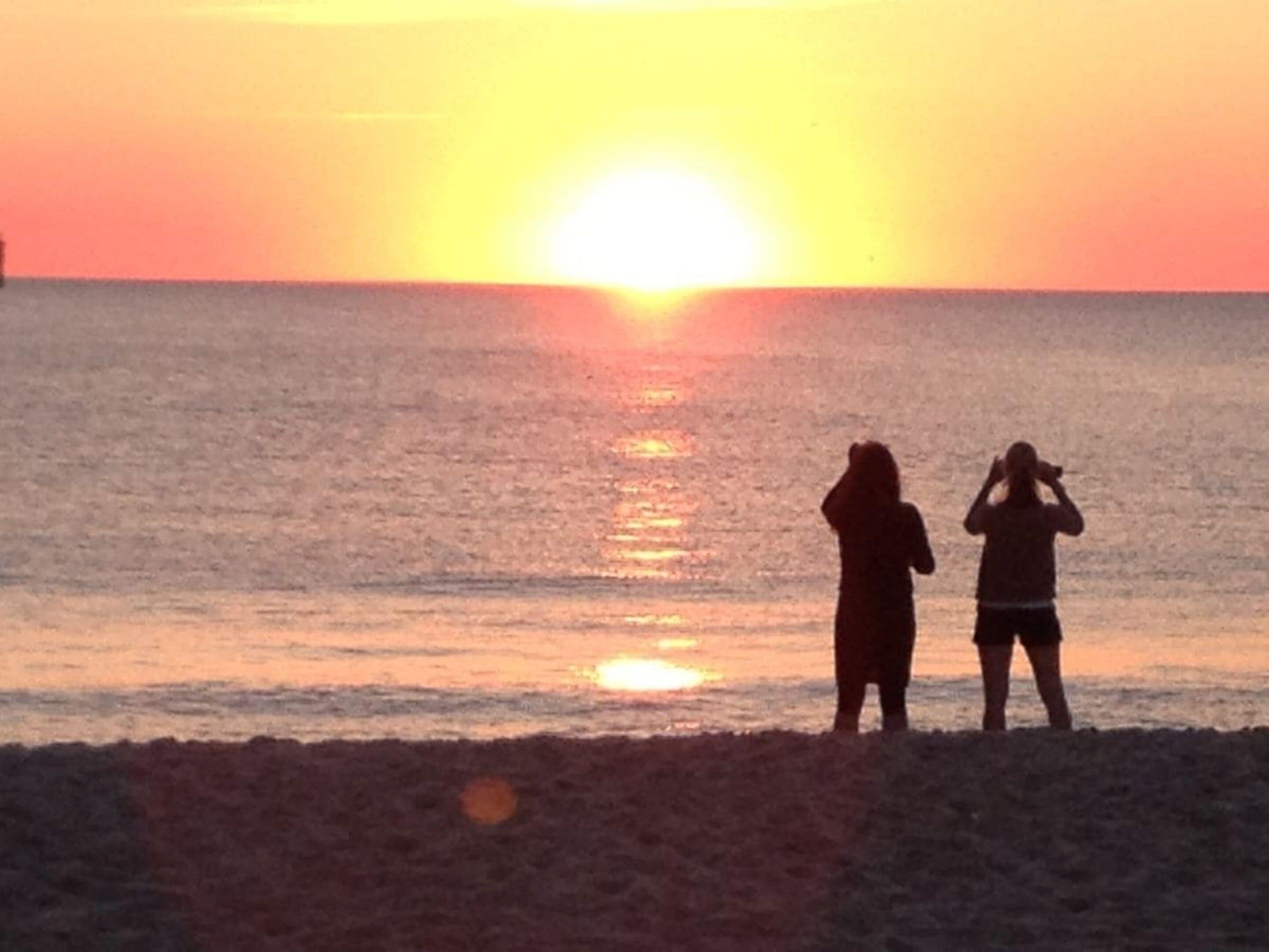 Silhouetten von zwei Personen am Strand, die den Sonnenuntergang betrachten.