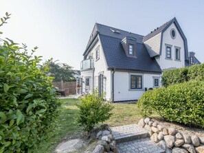 A two-story house with a stone pathway leading to the entrance, surrounded by greenery and a fenced yard. - Holiday Apartment in Westerland With Sauna (Sylt)