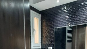 Un bagno moderno con una parete rivestita in piastrelle nere, un lavandino bianco e uno specchio.