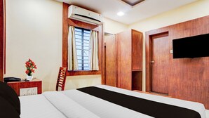 A hotel room with a bed, a desk with a telephone, a chair, an air conditioning unit, a window with curtains, and a wardrobe. - Townhouse Madan Mahal Railway Junction (Jabalpur)