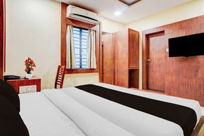 Habitación de hotel con cama, escritorio con teléfono, silla, equipo de aire acondicionado, ventana con cortinas y armario.