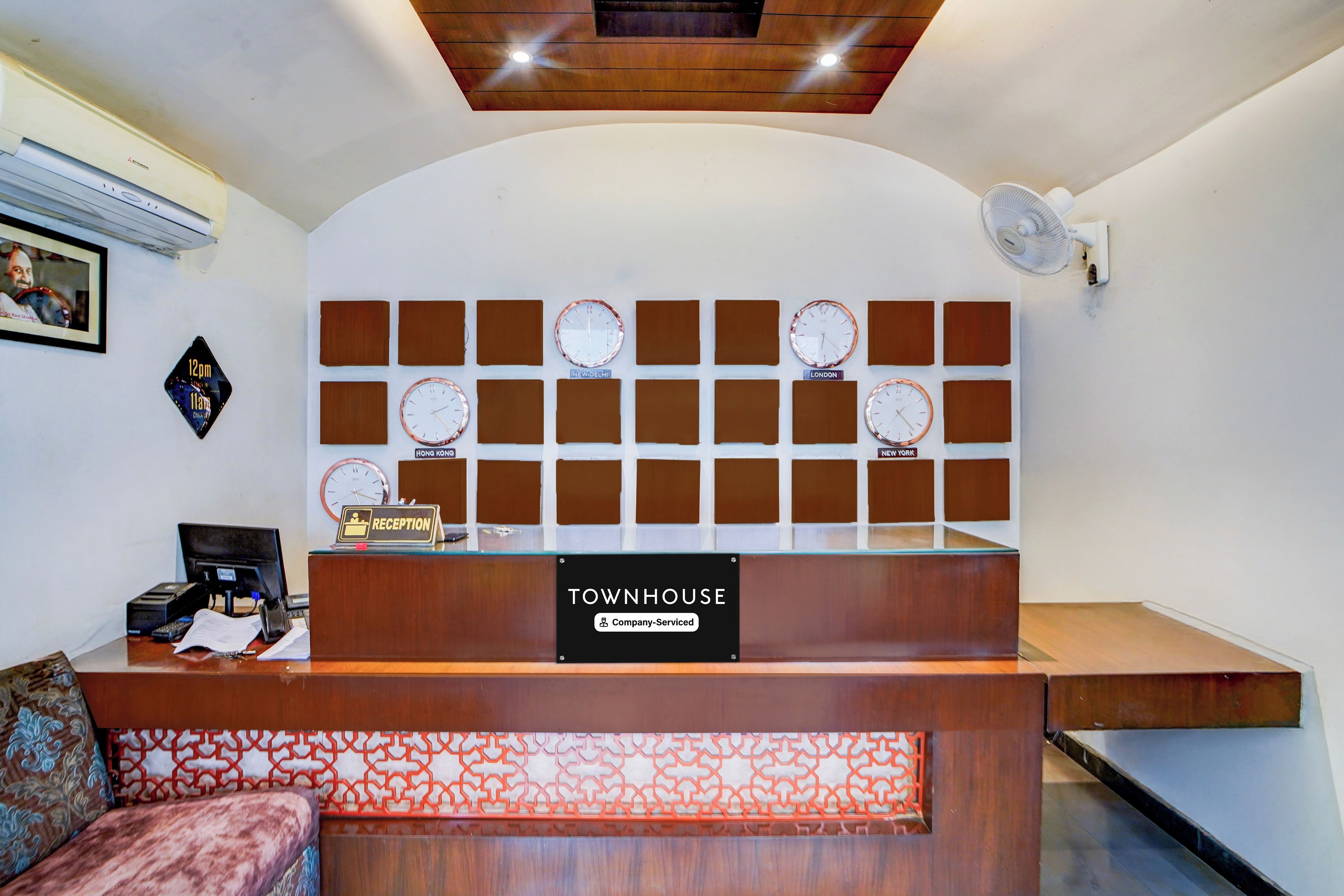 A reception desk with a sign indicating it is company-serviced. There are clocks displaying times from New Delhi, London, Hong Kong, and New York.