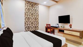 Una habitación de hotel con cama, escritorio, silla, televisor y ventana con cortinas.