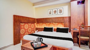 A hotel room with a wooden headboard, a bed with white and black bedding, a small wooden table with a tray of items, and a desk with a chair. - Townhouse Madan Mahal Railway Junction (Jabalpur)