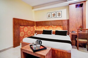 Habitación de hotel con cabecera de madera, cama con ropa de cama blanca y negra, una pequeña mesa de madera con una bandeja de objetos y un escritorio con una silla.
