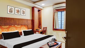 A hotel room with a bed, a desk, a chair, a window with curtains, and wall art. - Townhouse Madan Mahal Railway Junction (Jabalpur)
