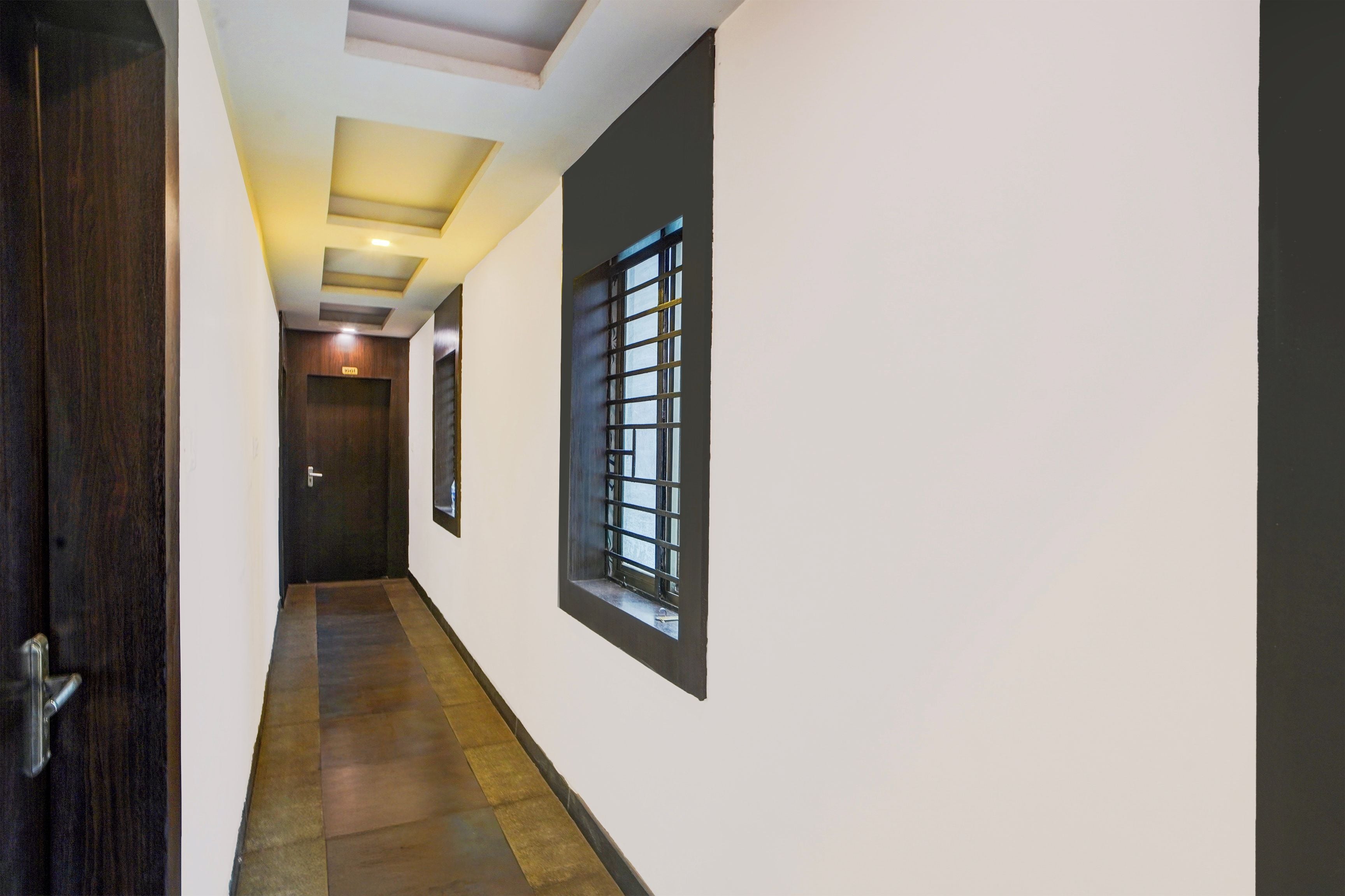A hallway with a wooden door, a window with bars, and a ceiling with recessed lighting.