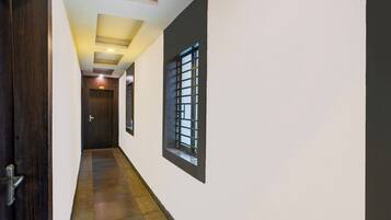 A hallway with a wooden door, a window with bars, and a ceiling with recessed lighting.