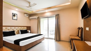 A hotel room with a bed, a desk, a chair, a TV, an air conditioning unit, a ceiling fan, and a balcony with curtains. - Townhouse Puri Shri Jagannatha Temple (Puri)