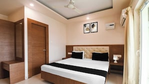 A hotel room with a bed, a nightstand, a mirror, a ceiling fan, and a window with curtains. - Townhouse Puri Shri Jagannatha Temple (Puri)