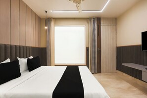 Habitación de hotel moderna con una cama grande, un televisor de pantalla plana y un ventanal con cortinas.