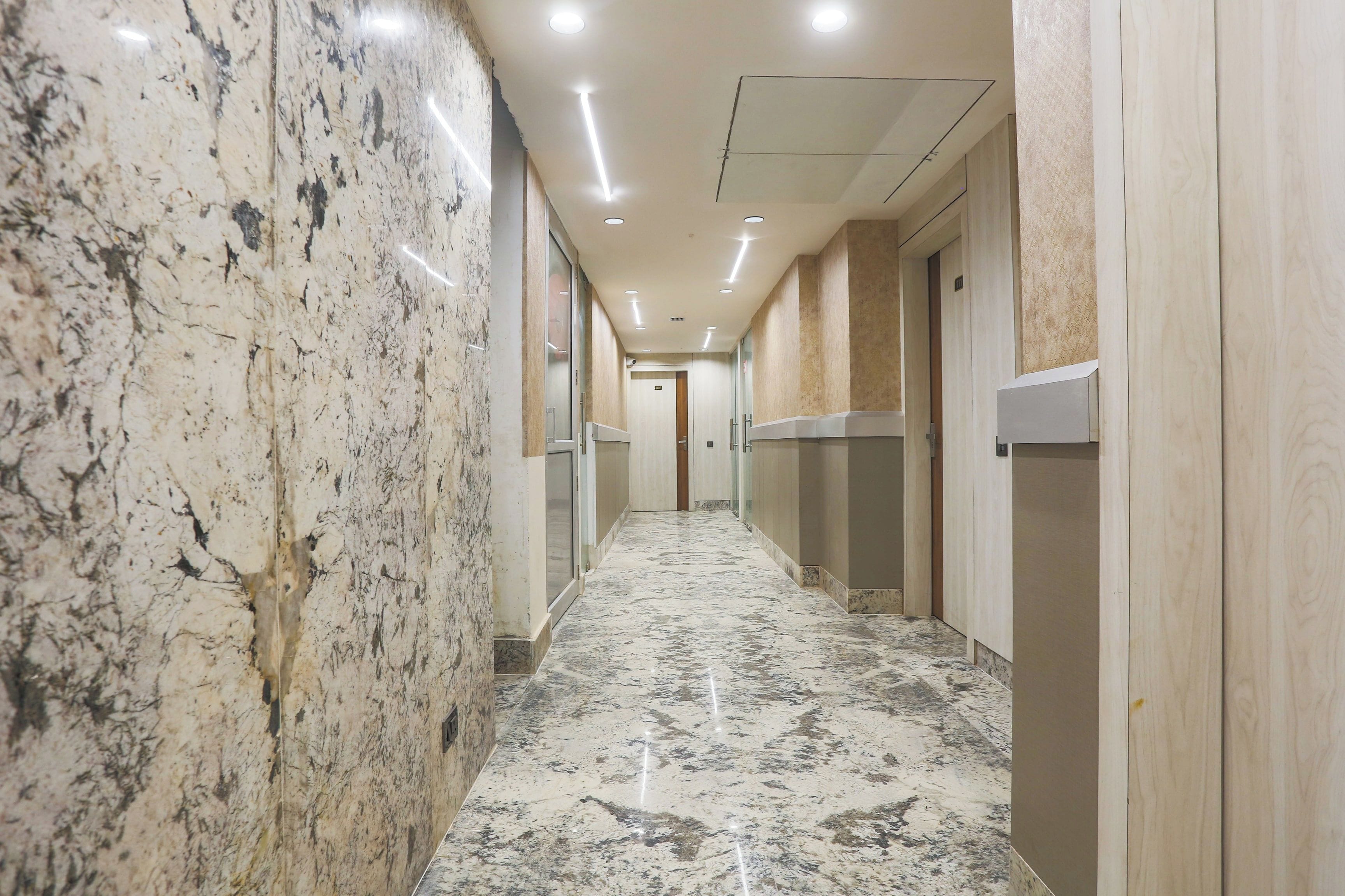 A corridor with marble flooring, recessed lighting, and doors on both sides.
