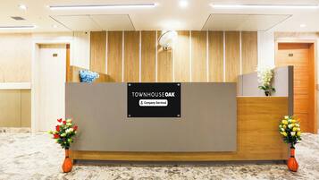 Ein Empfangsschalter mit Firmenlogo, flankiert von zwei Blumenarrangements, und eine Wand aus Holzverkleidung im Hintergrund.