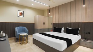 Habitació d'hotel moderna amb un llit gran, una zona de seients amb una cadira, una taula de nit i un armari.