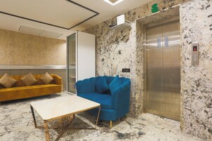 A lobby with a marble floor, a blue sofa, a wooden table, and an elevator.
