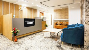 Zona d'acollida amb un taulell de recepció de fusta, una butaca blava, un sofà i una taula petita.