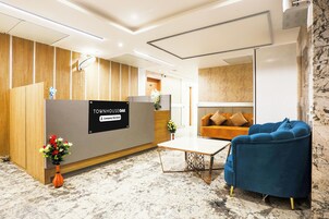 Un área de recepción con un mostrador de madera, un sillón azul, un sofá y una pequeña mesa.