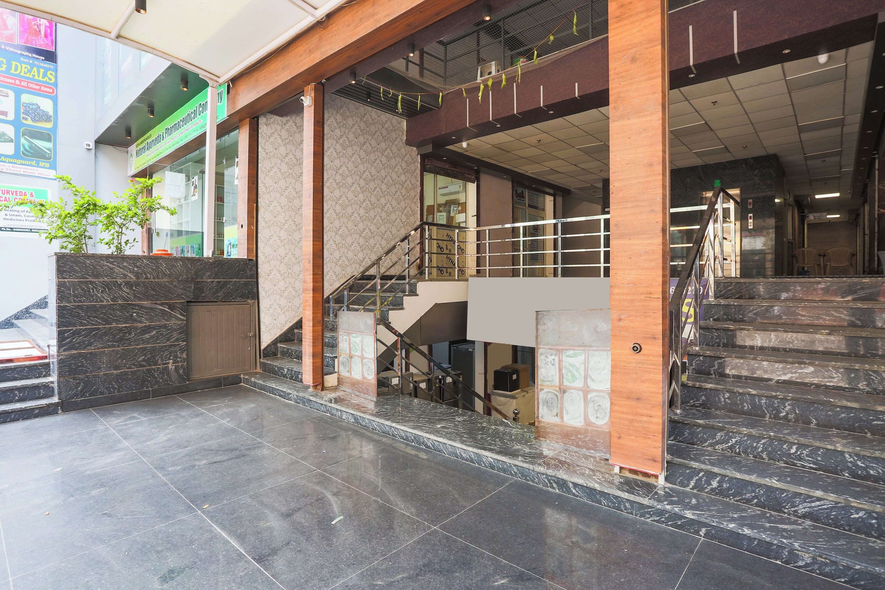 A commercial building with a staircase, marble flooring, and a green signboard.