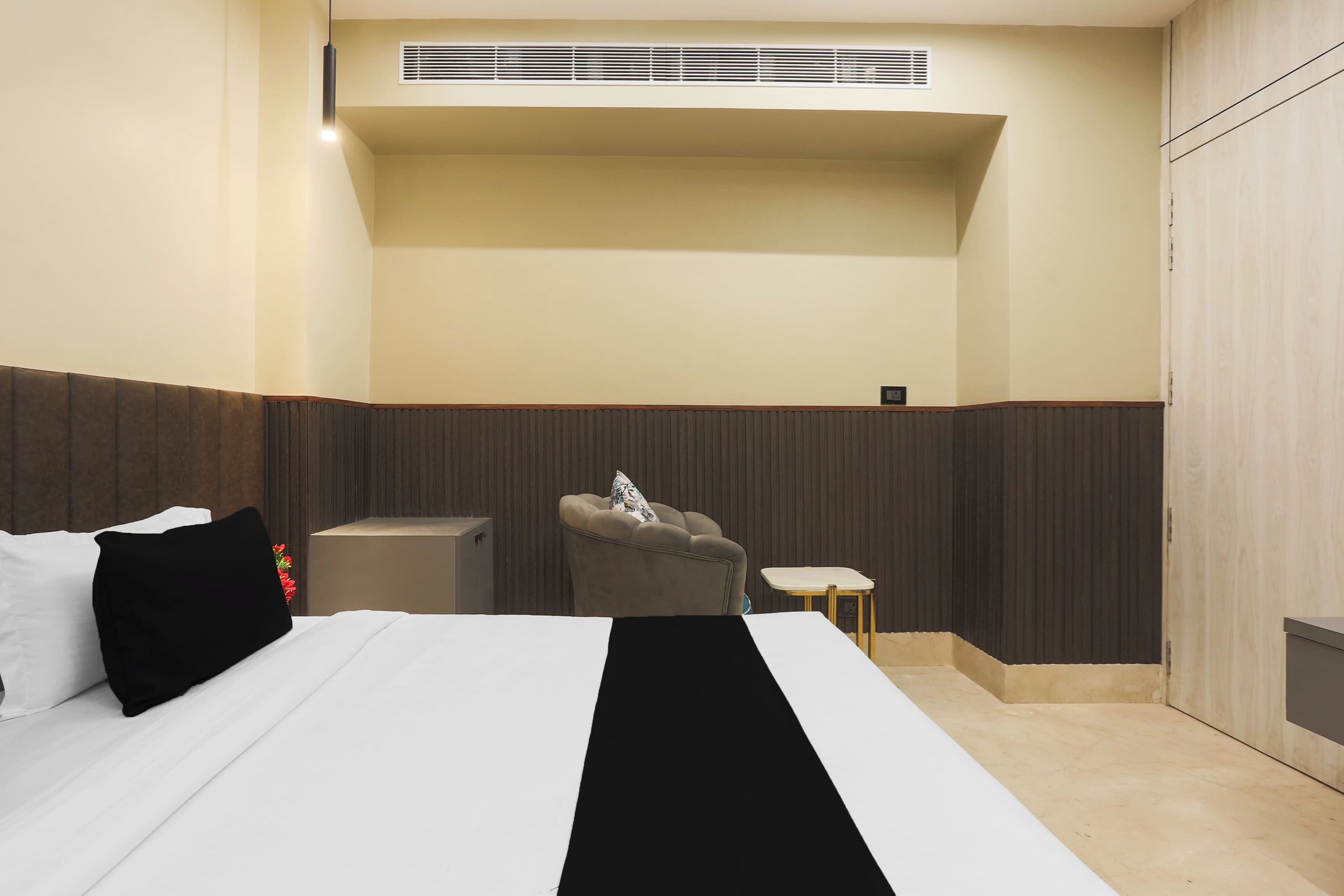 A hotel room with a bed, a small table, a chair, and a wall-mounted heater.