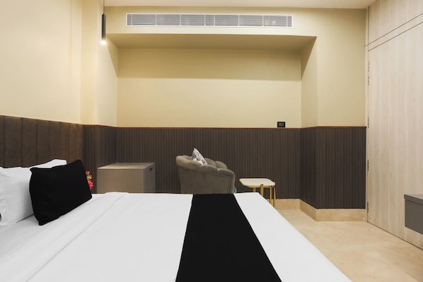 A hotel room with a bed, a small table, a chair, and a wall-mounted heater.