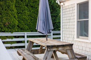 A wooden picnic table with a grey umbrella on a deck with a white fence and a green hedge in the background. - Yarmouth Port Oasis Near Ocean and Beach Fun (Yarmouth)