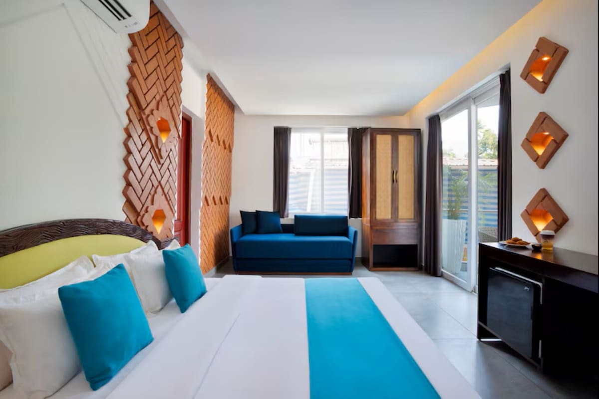 Quarto de hotel com cama, sofá, escrivaninha e vista para o exterior.