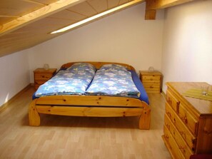 Ein Schlafzimmer mit einem hölzernen Bett, zwei Nachttischen, einer Kommode und einer geneigten Decke.