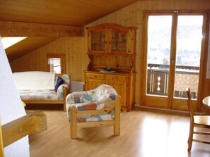 Ein gemütliches Zimmer mit Holzboden, einem Bett mit farbenfroher Steudecke, einer Holzkommode mit Glastüren und einem Balkon mit Blick.