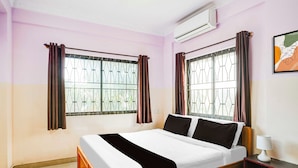 A bedroom with a bed, a nightstand, an air conditioner, and a window with curtains. - Townhouse Bangalore Goraguntepalya (Bengaluru)