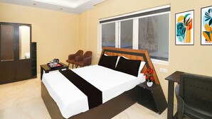 A hotel room with a bed, a desk, a chair, a window, and artwork on the wall. - Townhouse Ranchi Tapovan Mandir (Ranchi)