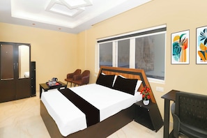 Una habitación de hotel con cama, escritorio, silla, ventana y cuadros en la pared.